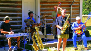 Wilbur Rehmann Quintet performing outside in front of a log cabin